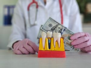 model of a dental implant and a dentist holding money beside it